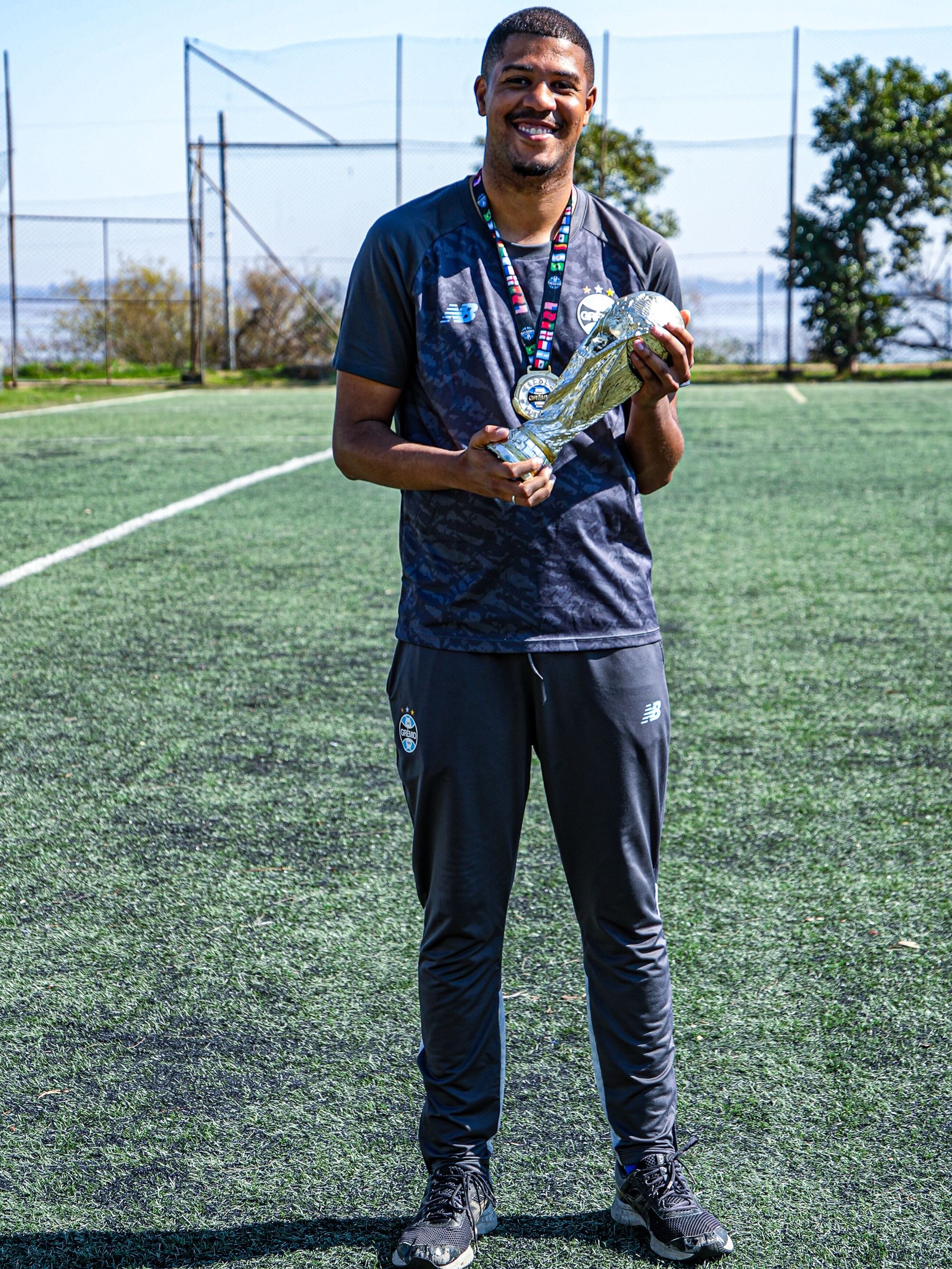 Luan Garcia com medalha e troféu em um campo de futebol
